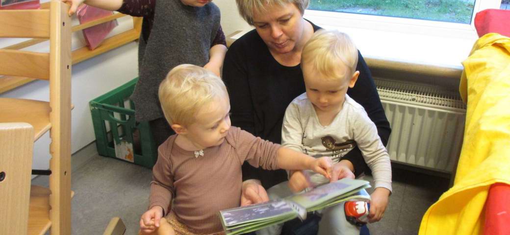 Børn kigger i bog sammen med pædagog